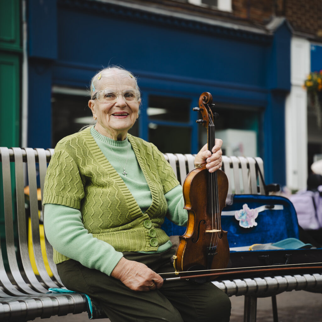 Portrait by Steven Hatton of a Boston resident seated outdoors holding a violin, part of The Bostonians community exhibition