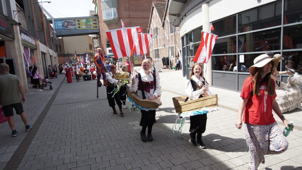 Boston Hanseatic Day parade with participants wearing Hansekoggen boat costumes and carrying red and white ship sails through the town centre