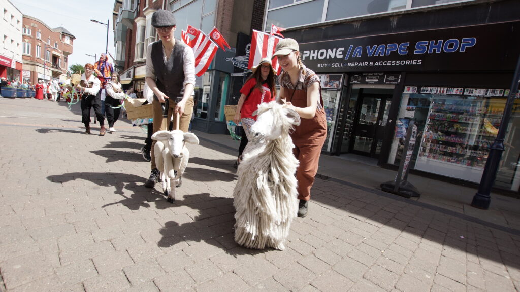 Puppet performers leading a Lincolnshire Longwool sheep and lamb through a busy high street during a free family-friendly event in Lincolnshire