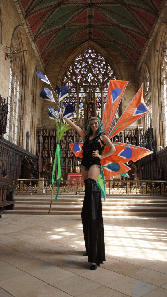 Performer and stiltwalker wearing large skullcap flower costume with orange panels inside historic church interior in Boston Lincolnshire