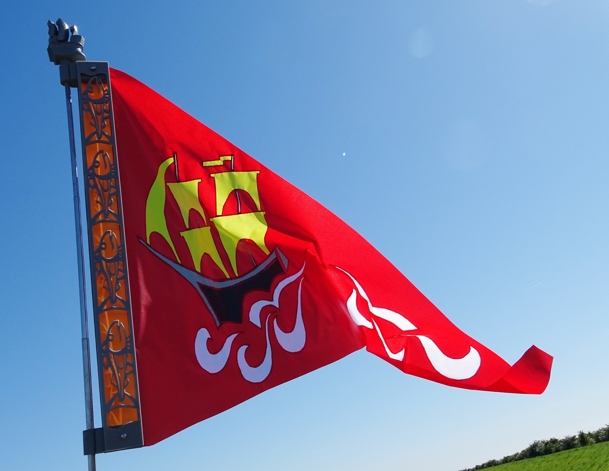 Bright red Boston Unfurled flag with stylised medieval ship design flying on pole against blue sky in Boston, Lincolnshire