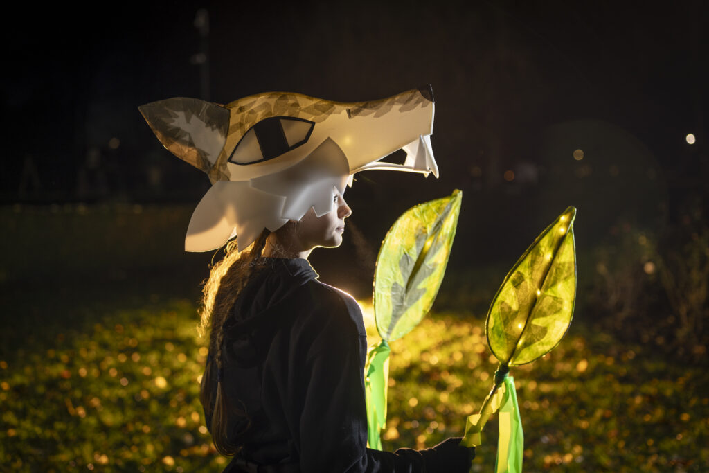 Participant wearing illuminated animal head costume and carrying glowing leaf lanterns during an outdoor Illuminate parade event in Boston Lincolnshire