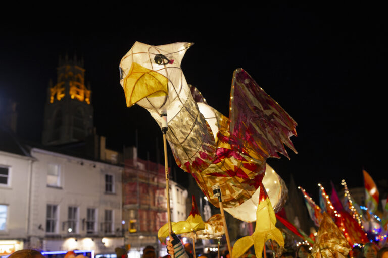 Illuminated Griffin lantern puppet held above a crowd at night during Boston’s Illuminate parade