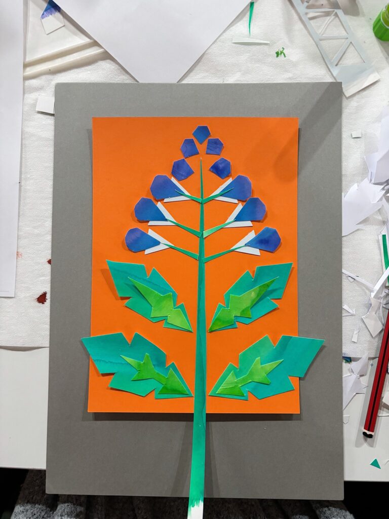 Hanseatic-inspired paper collage of a skullcap flower design made with layered coloured shapes on orange background during community art workshop