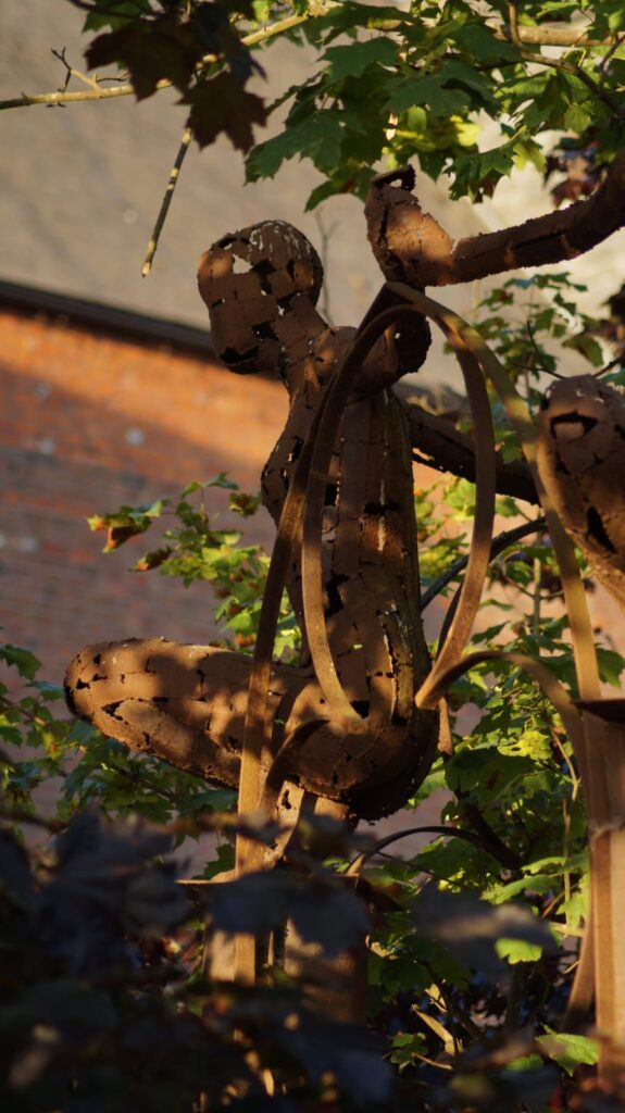 A metal sculpture of a person in a hoop hanging by a tree