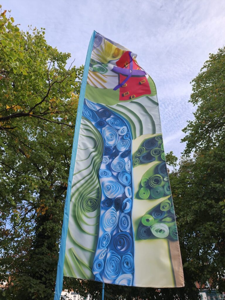 A close up of a colourful feather flags featuring designs of a river and a pink windmill on a roadabout in Boston