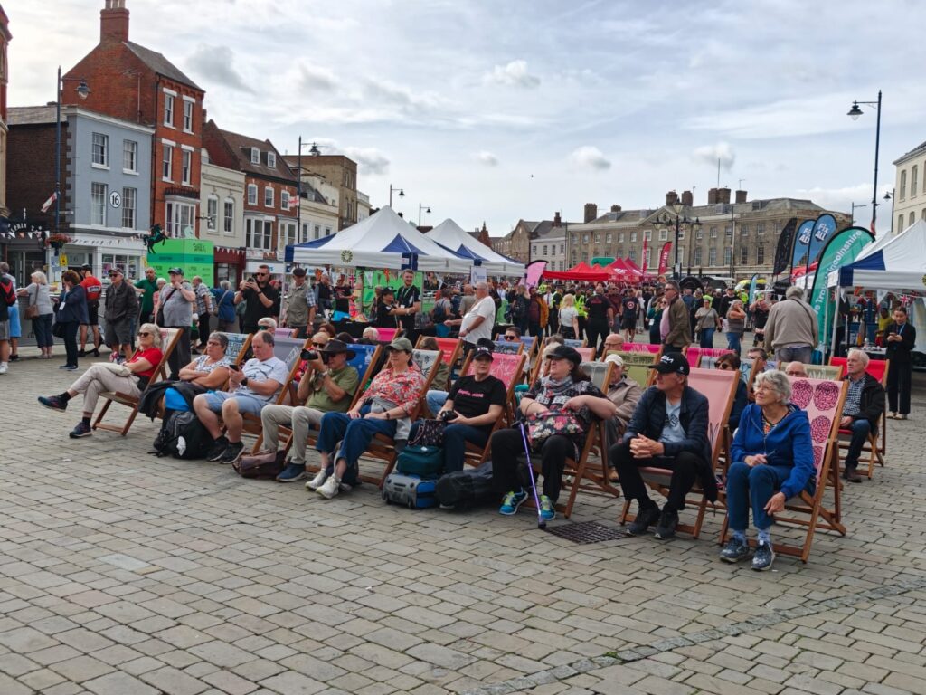 Crowds sit on colourful Transported deckchairs to watch the live video footage screening of the Tour of Britain race in Boston Market Square