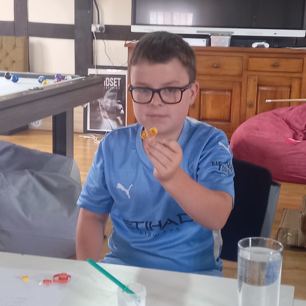 A young male participant creates colourful flag designs with marker pens and rolled paper in a method called quilling and holds it up to the camera