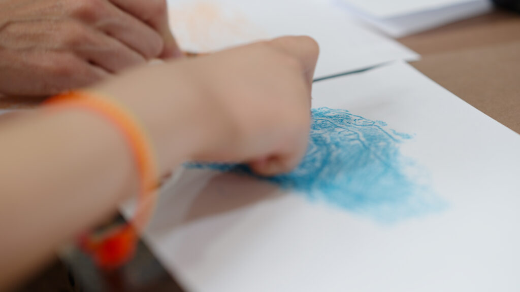 A close up image of a child using a blue crayon to create a brass rubbing picture