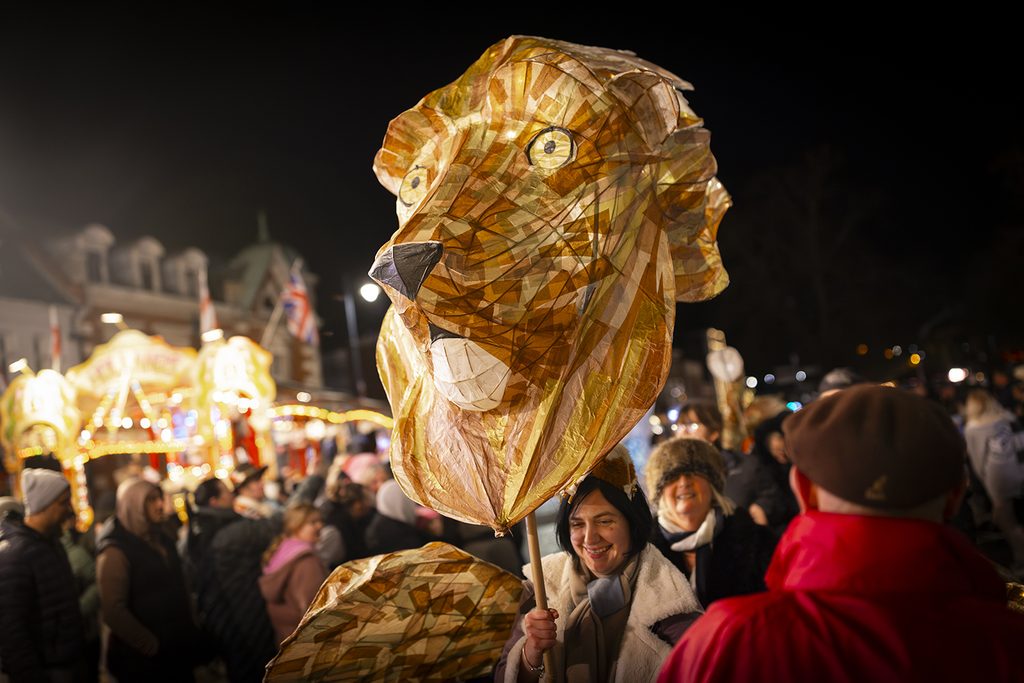 A giant illuminated lion head lantern is paraded through busy evening streets of Boston