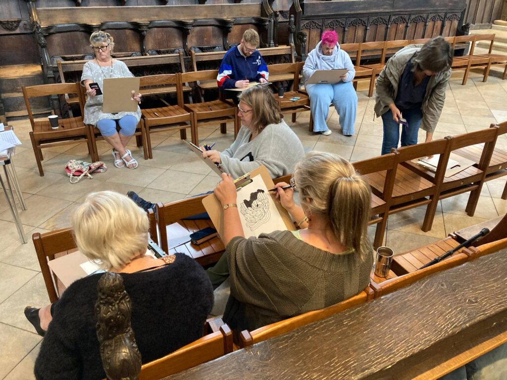 Several people sit on chairs in St Botolph's, sketching