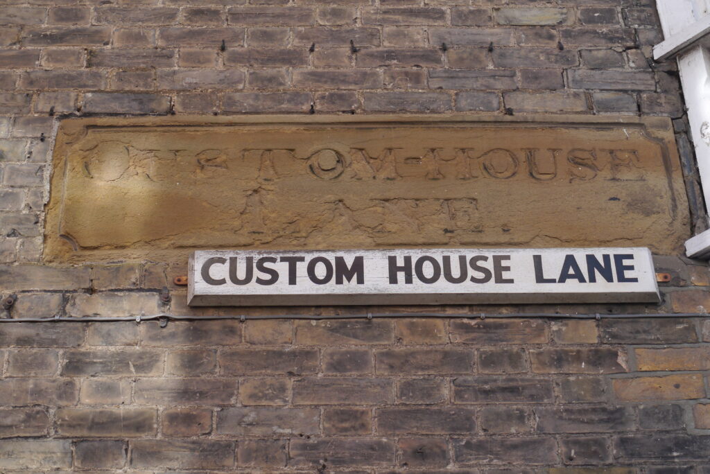 Custom House Lane modern street sign beneath vintage stone signage