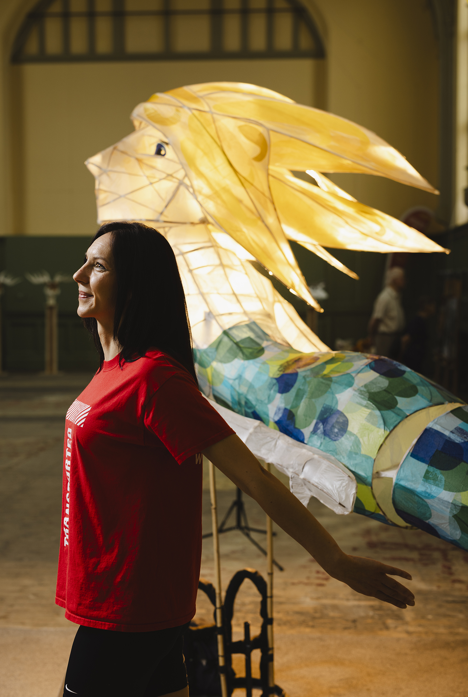 A woman poses with her arms outspread next to a giant illuminated mermaid lantern