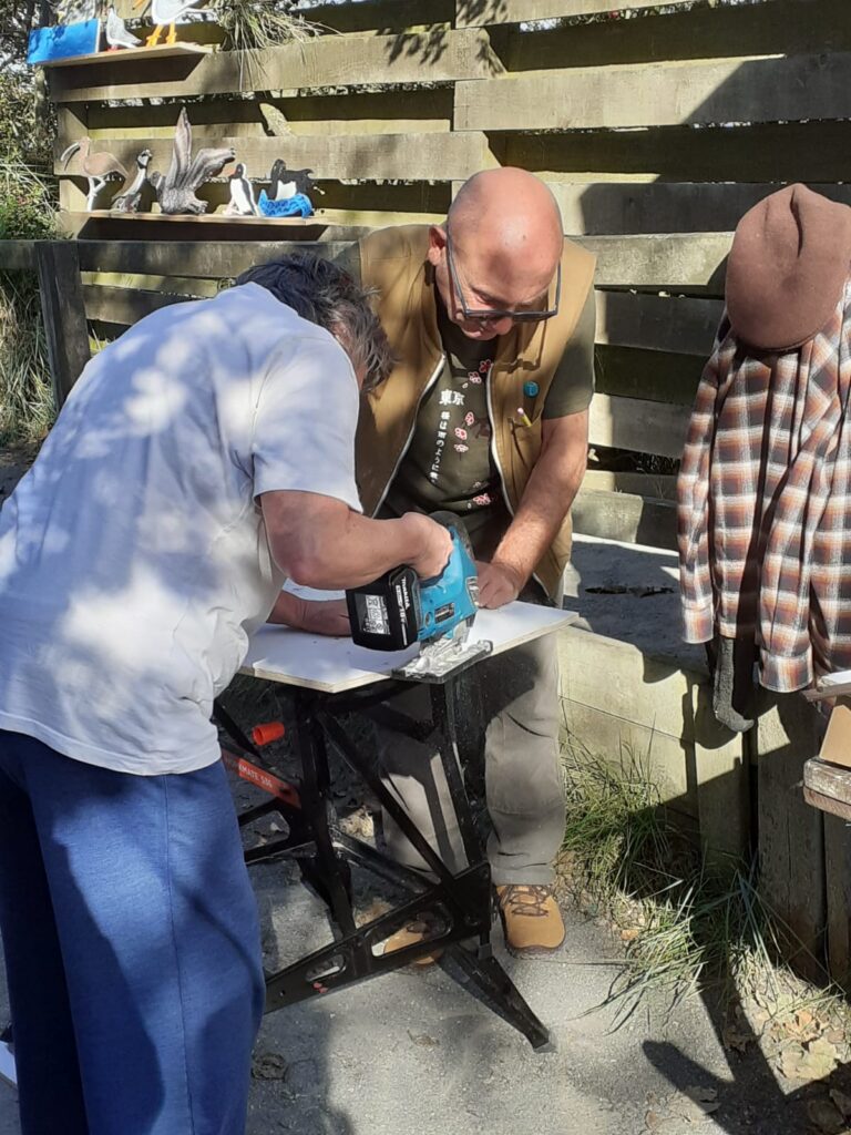Participant using a jigsaw to cut a bird-shaped wooden waymarker during a community art workshop at RSPB Freiston Shore.