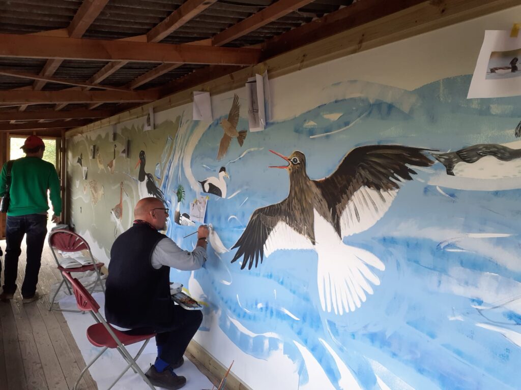 Artist Chris Lewis Jones painting the wildlife-inspired Flyways mural inside the refurbished bird hide at Freiston Shore.
