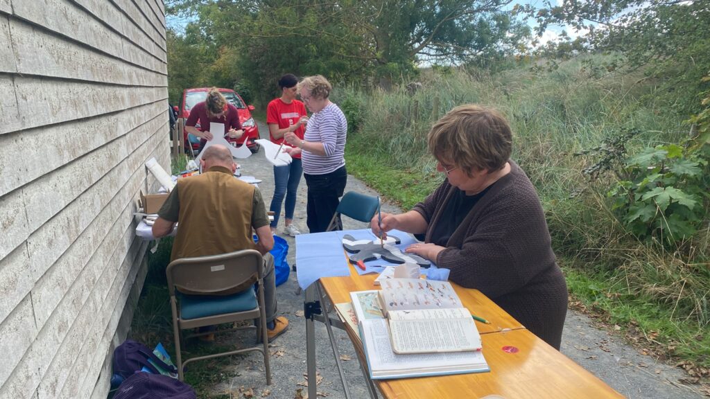 Participants paint bird-shaped wooden waymarkers during a community art workshop at RSPB Freiston Shore.