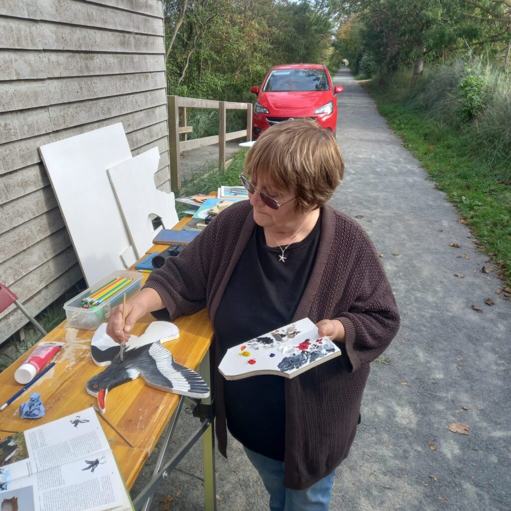 A participant paints bird-shaped wooden waymarker during a community art workshop at RSPB Freiston Shore.