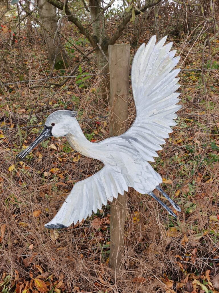 Hand-painted heron waymarker installed beside a wetland path at RSPB Freiston Shore Nature Reserve.