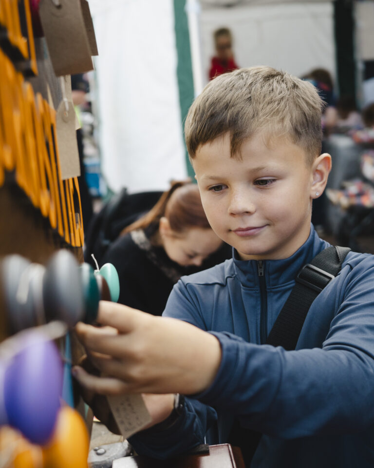 An image of a young boy exploring the Cabinet of Curiosities, hanging a tag with his comment on to one of the cabinets' colourful handles