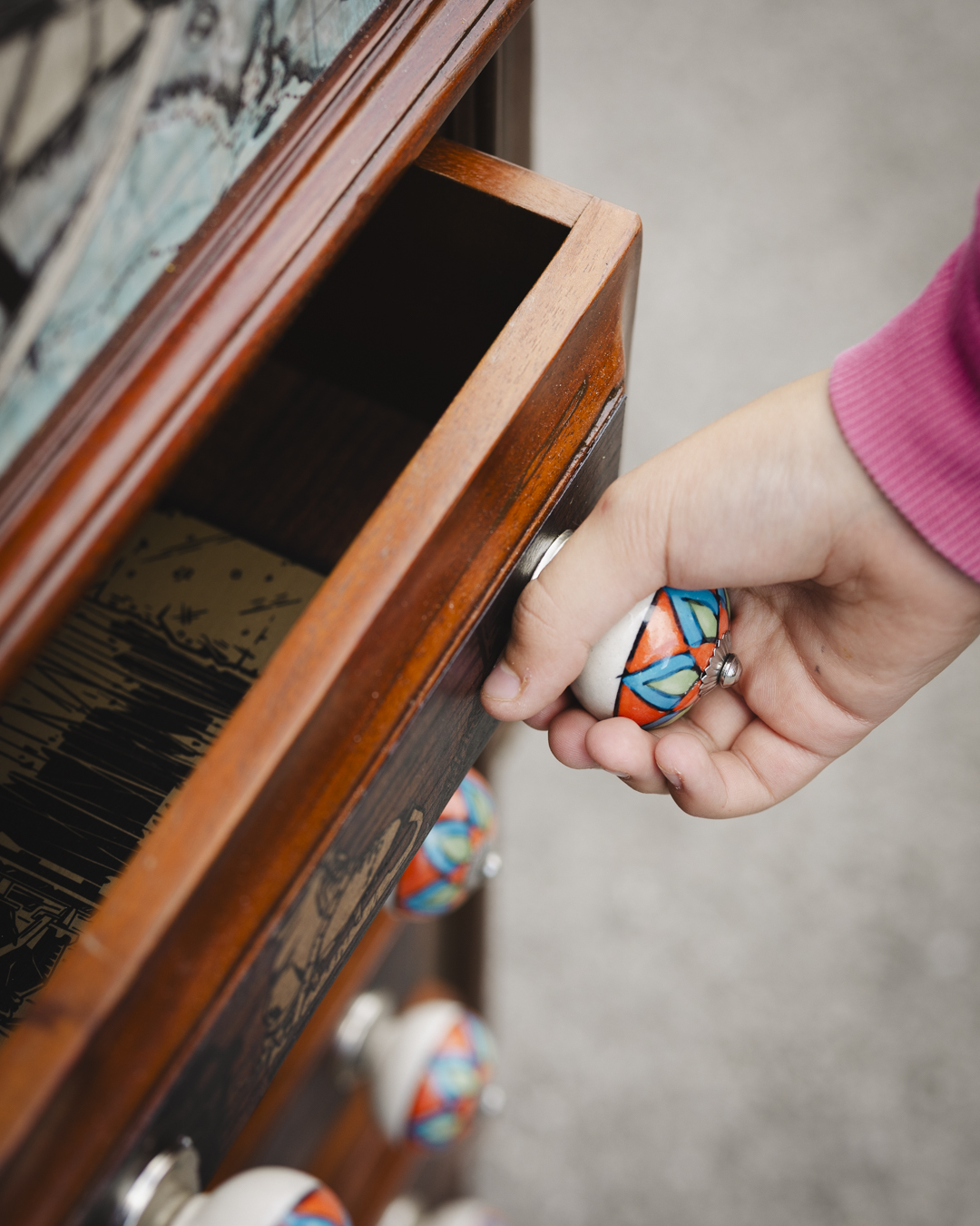 A close up image of a child pulling an ornate colourful handle and opening one of the interactive drawers of the Cabinet of Curiosities