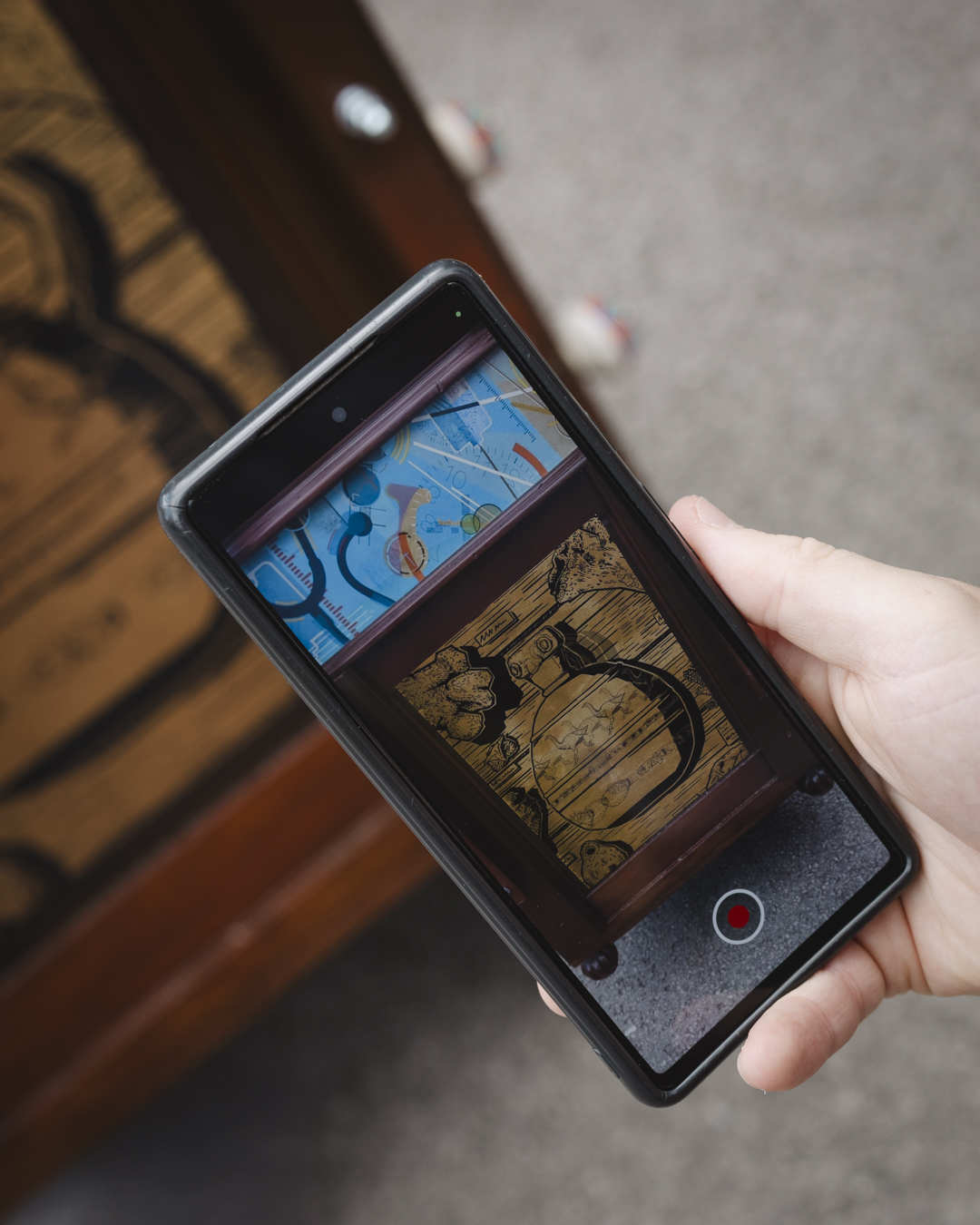 A close up image of a participants hand using a phone and app to animate an ARTeFACT trail artwork on the Cabinet of Curiosities. The ARTeFACT trail is an augmented-reality trail in Spalding Lincolnshire inspired by items in the Spalding Gentlemen Society's museum collection