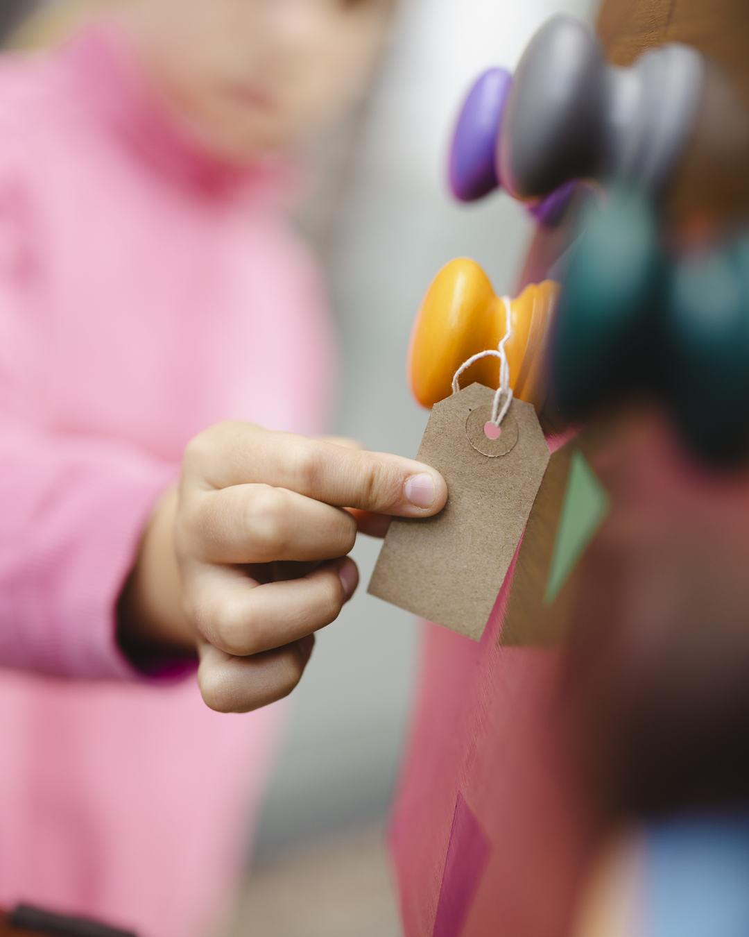 A close up image of a child hanging a brown label to one of the Cabinet of Curiosities colourful interactive knobs
