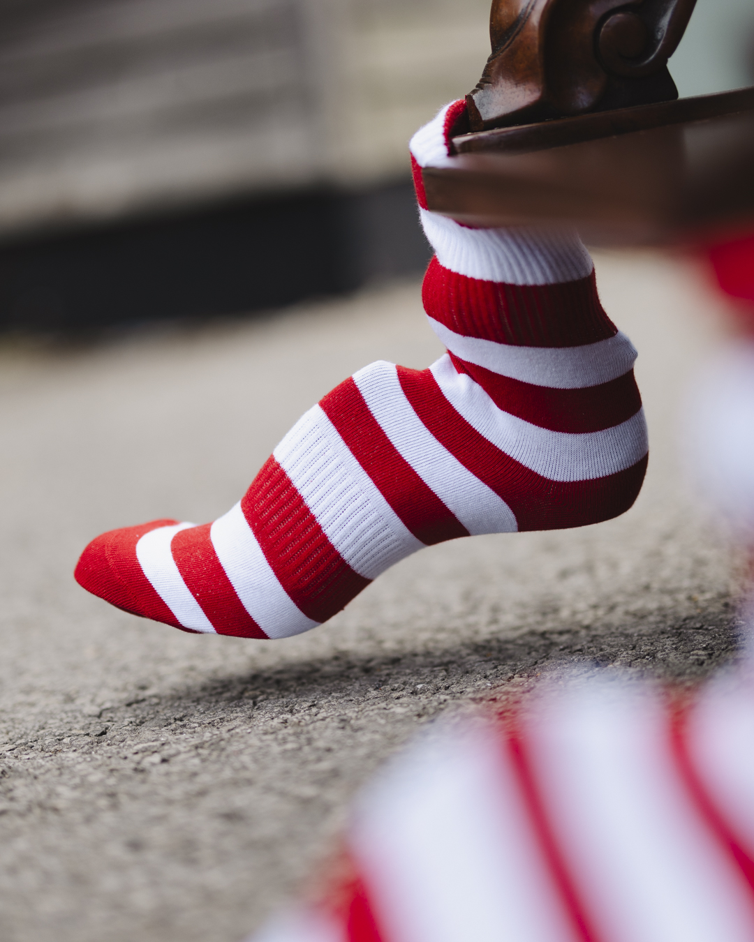 A close up image of one of the Cabinet of Curiosities decorative wooden feet adorned in a jolly white and red striped sock
